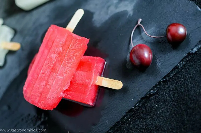 red Alcoholic popsicles with cherries on a slate with cherries