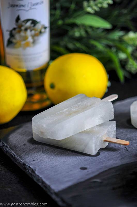 Alcoholic popsicles on a slate with lemons and simple syrup bottle