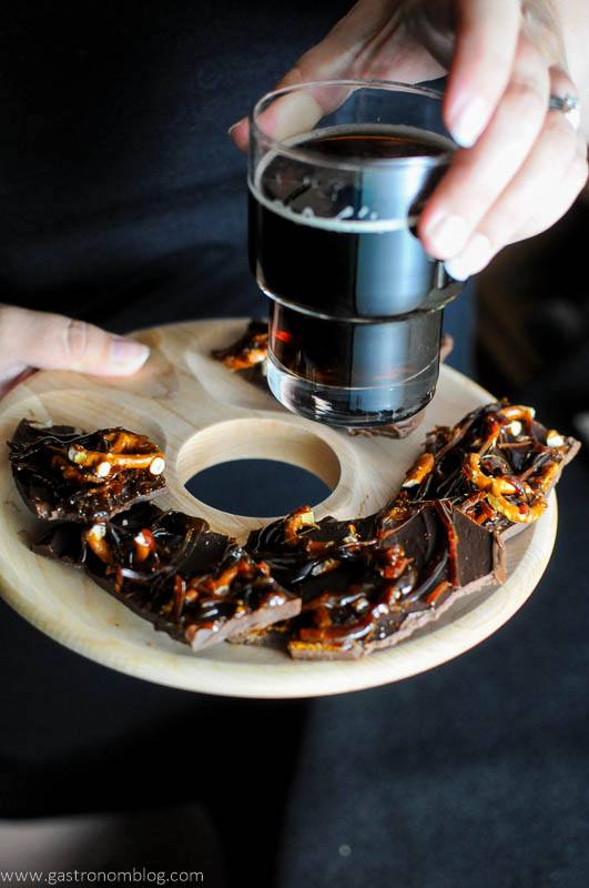 Beer Brickle Chocolate Bark dessert - on a wooden tray with hand holding a dark beer
