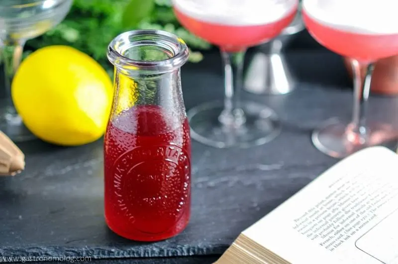 Rich Raspberry Simple Syrup - pink syrup in jar. Lemons, flowers and pink drinks with white foam in coupes