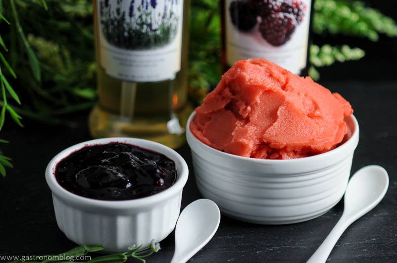 Two frozen sorbets, 1 purple, 1 pink, simple syrup bottles and flowers in background