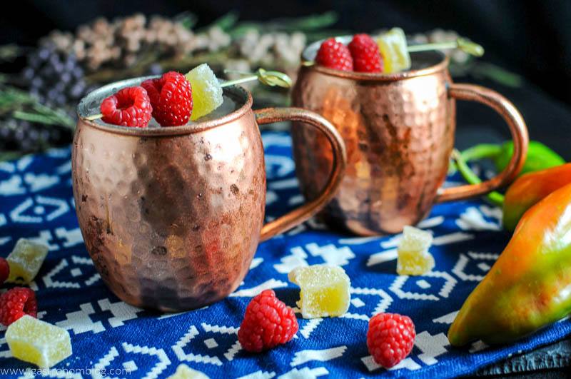 Hatch Chille and Raspberry Moscow Mule in copper mug with crystallized ginger and raspberries on blue and white napkin