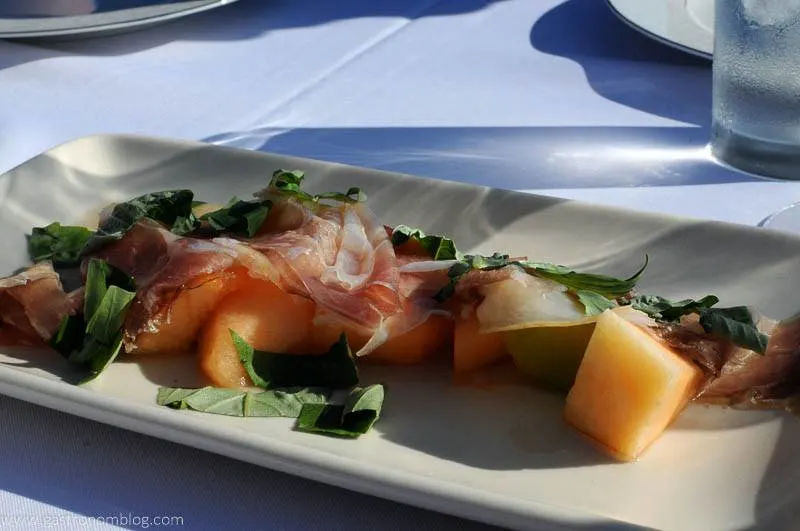 melon and prosciutto with greens on white plate