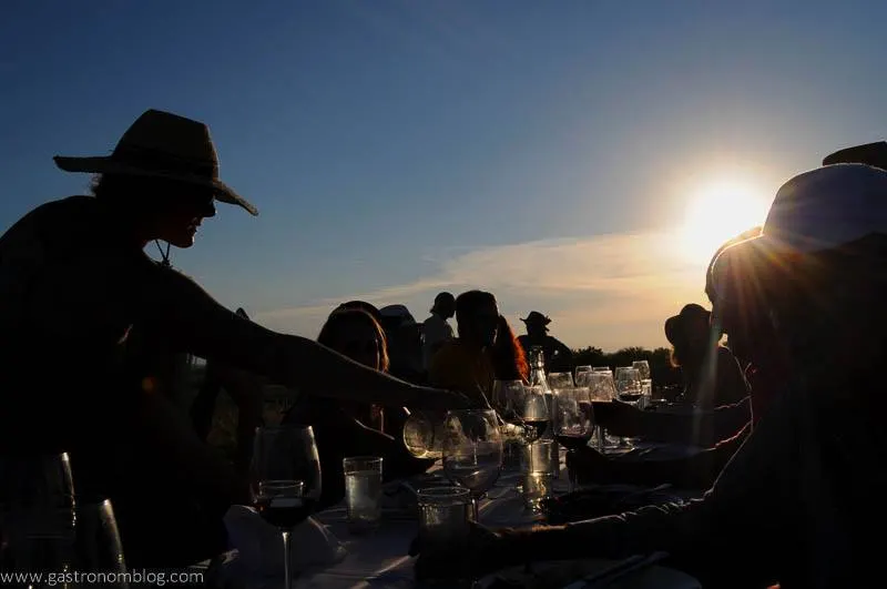 People seated at a long table at sunset, their silhouettes are showing against the sun