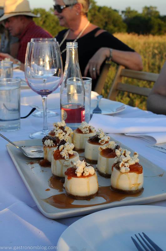 Goat cheese and caramel tarts topped with popcorn on a white plate, wine glasses and people behind