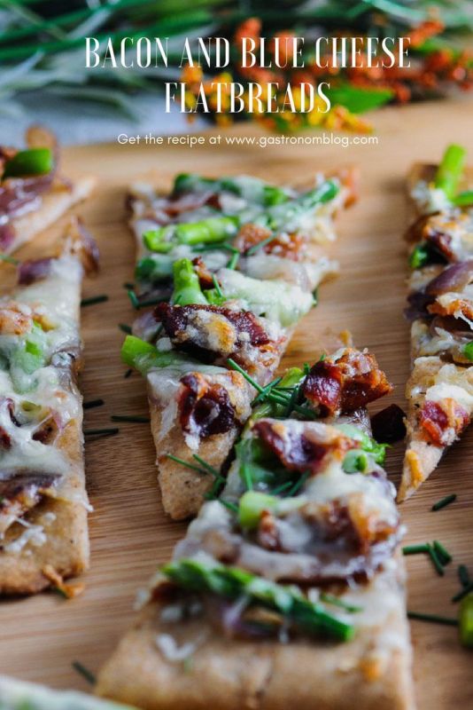 Bacon, blue cheese and asparagus flatbreads on wooden board, flowers behind
