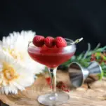 Pink cocktail in coupe with raspberries, on wood with flowers behind