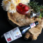 Pink cocktail in coupe, top shot of white vermouth bottle on wood, flowers