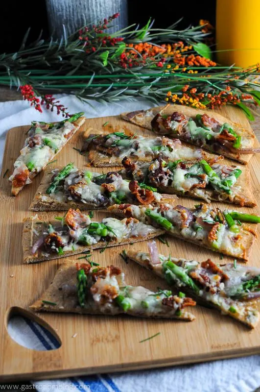 Bacon and Blue Cheese Flat Breads on wood cutting board. White napkin and flowers in background