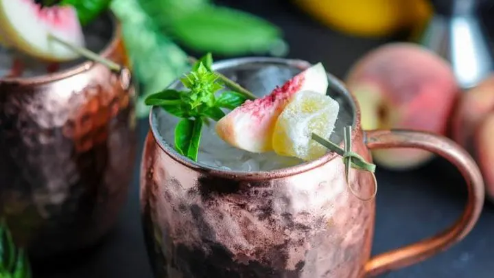 Peach and Basil Moscow Mule in copper mule with peach slice, candied ginger and basil sprig