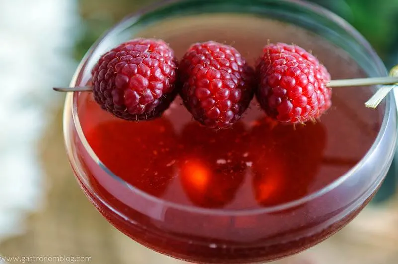 Raspberry Manhattan Cocktail in coupe glass with raspberries on cocktail pick