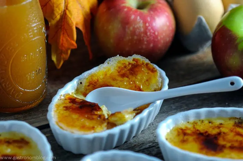 apple Creme brulee in white ramkeins, apples, fall leaves and brandy bottle behind