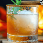 Autumn Pear Cocktail, brown cocktail in rocks glass with ice ball, cinnamon sticks and rosemary sprig