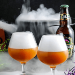 Orange cocktails in snifters with dry ice clouds. Cauldron with dry ice and ginger beer bottle in back