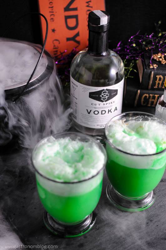 Polyjuice Potion - a green vodka cocktail in glass mugs. Vodka bottle and cauldron with dry ice in the background
