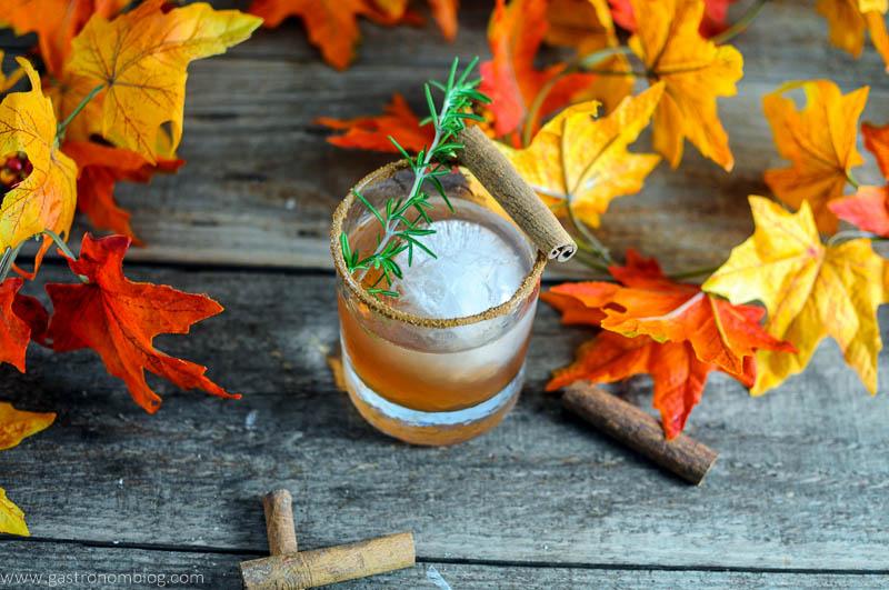 The Autumn Pear cocktail in rocks glass with cinnamon sticks and rosemary. Fall leaves