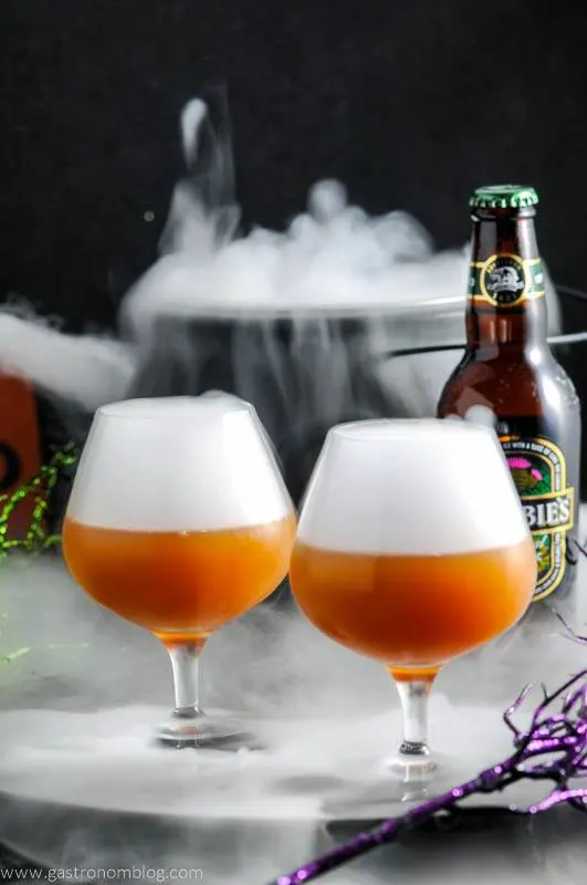 Orange Alcoholic Butterbeer Recipe in snifters with white fog on top, Halloween decor in background