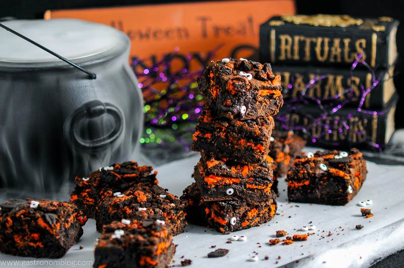 Halloween Oreo Monster Brownies on parchment paper with eyeballs, dry ice in cauldron behind with books and halloween signs