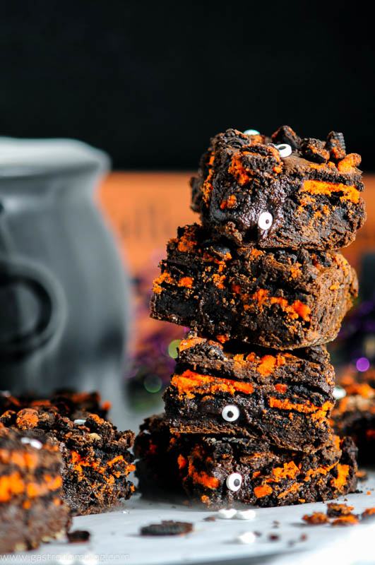 Halloween Oreo Monster Brownies in a stack on parchment paper. Cauldron behind