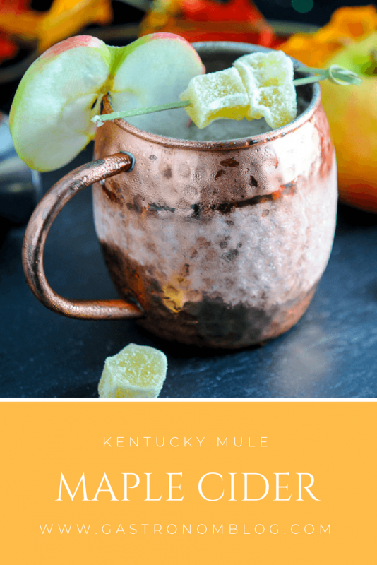 Maple and Cider Kentucky Mule in a copper mug with apple slice and candied ginger, autumn leaves behind