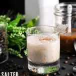 White russian in a cocktail glass, leaves, white bottle and sauce behind