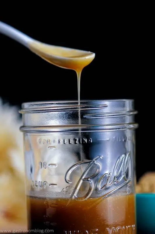 White ceramic spoon dripping Salted Bourbon Butterscotch Sauce into a mason jar