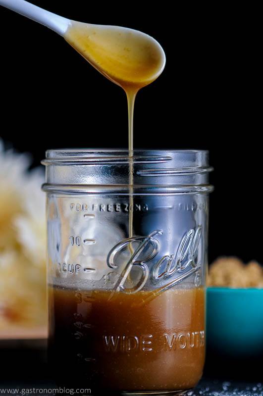 Salted Bourbon Butterscotch Sauce in jar, white spoon dripping into jar