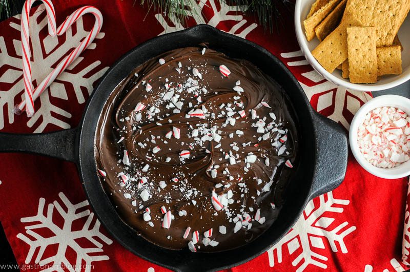 Candy Cane Skillet Smores with Boozy Marshmallows - chocolate and peppermint in skillet. Graham crackers and crushed peppermint in bowls. Red and white napkin
