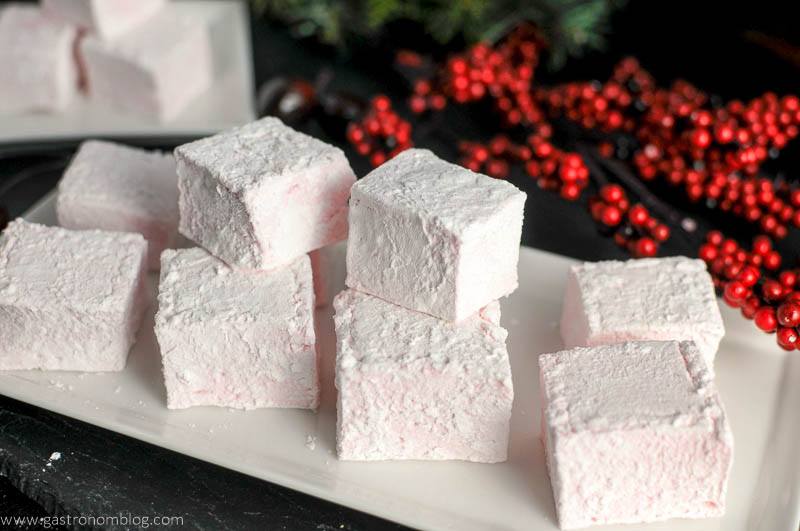 pink Marshmallows stacked on white plate, red berries on branch behind