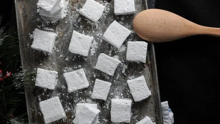 Peppermint Vodka and Kahlua Mocha Marshmallows cut in squares on a cookie sheet with wood spoon
