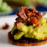Guacamole on sweet potato chips topped with bacon on white plate