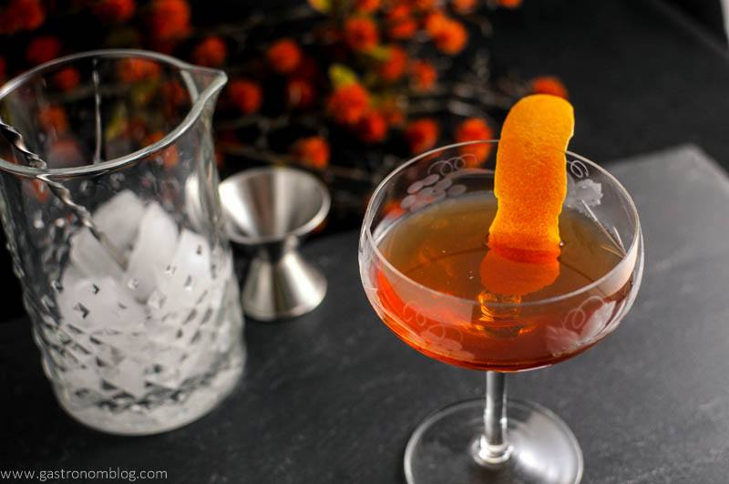 The Woodsman - An Apple Brandy and Ginger Cocktail in coupe with orange peel, mixing glass and bar spoon, jigger in background