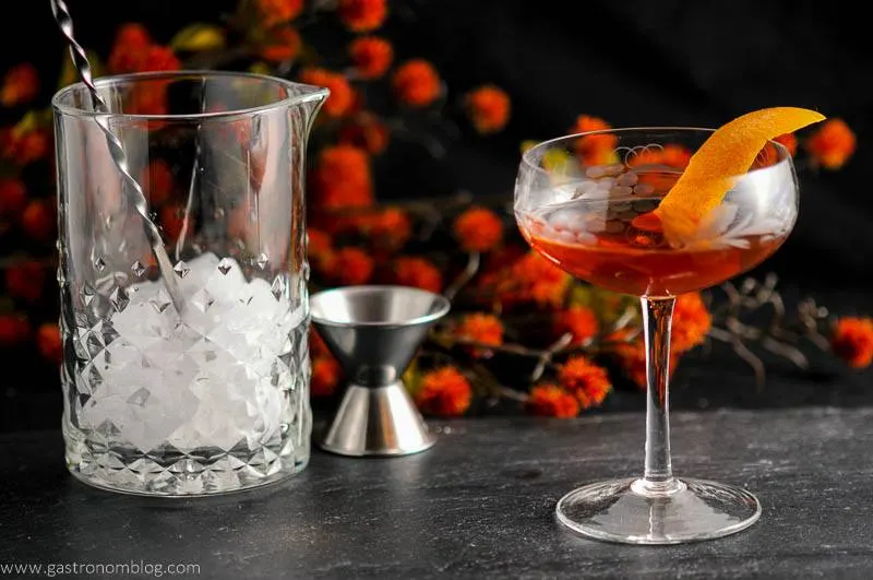The Woodsman - An Apple Brandy and Ginger Cocktail in a coupe, mixing glass and bar spoon, jigger and flowers in background