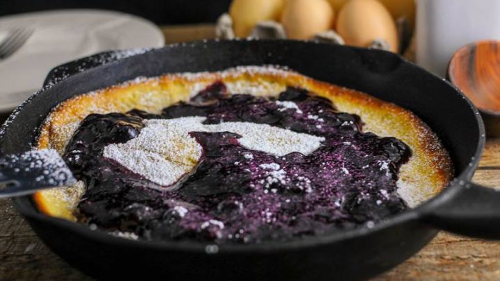 Dutch Baby Pancake with Blueberry Whiskey Sauce in skillet. Eggs and white jar in background