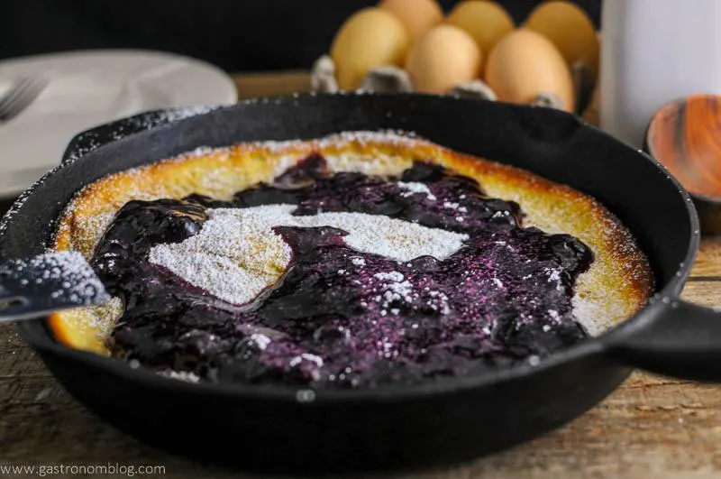 Dutch Baby Pancake with Blueberry Whiskey Sauce in skillet. Eggs in background