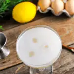 Top shot of egg white topped cocktail, eggs and lemon in background
