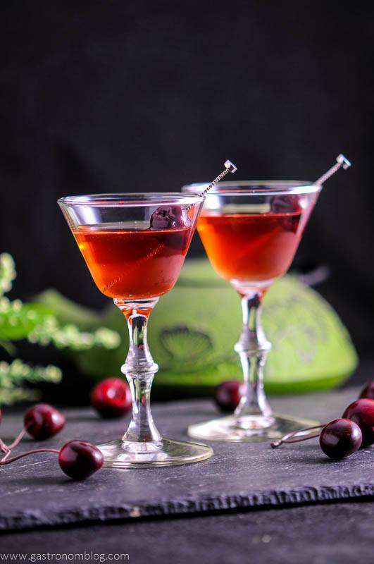 The Cherry Blossom Cocktail in two cocktail coupes with cherries and teapot in background