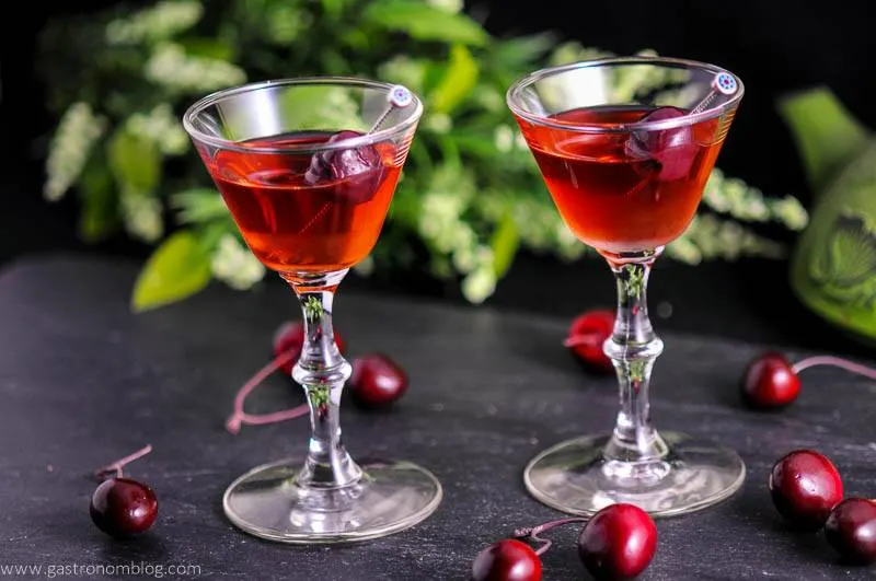 The Cherry Blossom Cocktail in two cocktail coupes with cherries and flowers in background