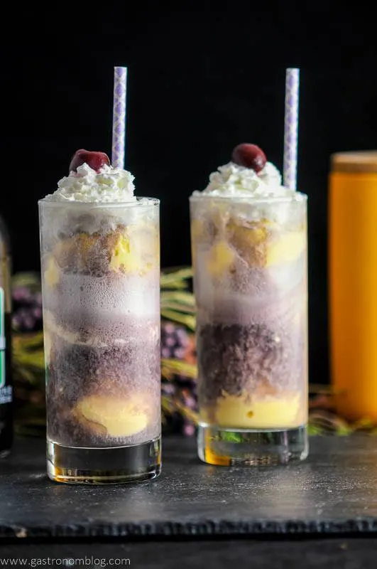 Adult Purple Cow with Nehi Grape Soda in 2 glasses with layers of ice cream and grapesoda, cherries and whipped cream on top with straws