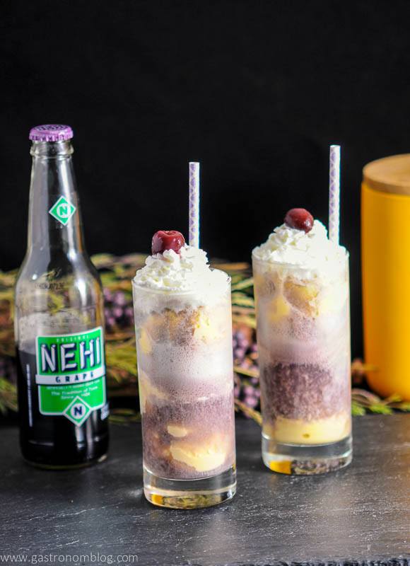 Adult Purple Cow with Nehi Grape Soda in highball glasses with straws, cherries and whipped cream. Grape soda bottle in background with flowers