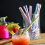 Pink cocktail with strawberries and pineapple, straws in mixing glass