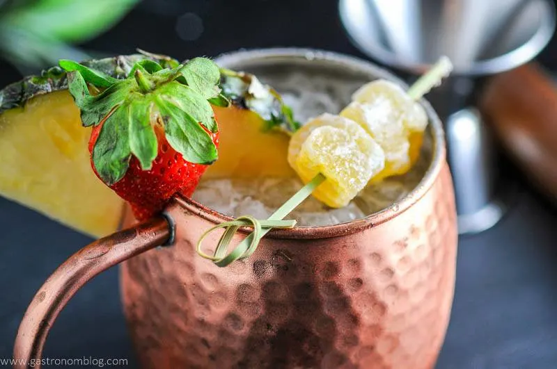 Spicy Pineapple Strawberry Moscow Mule in copper mug with strawberry, pineapple wedge and ginger. 