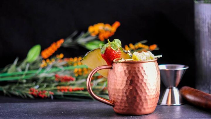 Spicy Pineapple Strawberry Moscow Mule in copper mug. Flowers and jigger behind