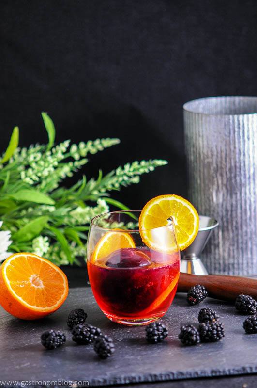 Blackberry Tangerine Vodka Tonic Cocktail, purple cocktail in glass with tangerine slices. Greenery and metal container in background