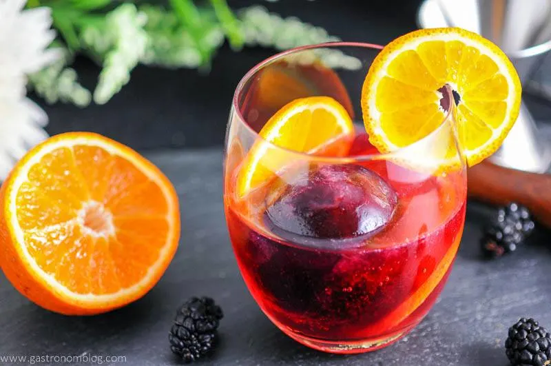 Blackberry Tangerine Vodka Tonic Cocktail with orange wheels. Orange half and flowers.
