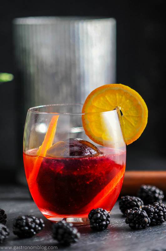 Blackberry Tangerine Vodka Tonic Cocktail in glass with orange wheel. Blackberries and metal container in background