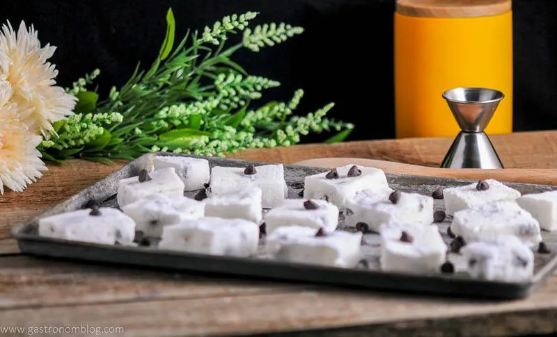 Chocolate Chip Boozy Marshmallows on cookie sheet. Jigger, flowers and yellow canister in background