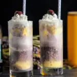 Purple ice cream float in tall glasses, white and purple straws, cherries and whipped cream
