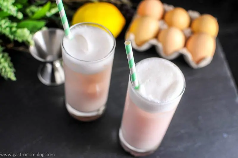pink cocktail in highballs. Lemon, jigger, flowers and eggs in background
