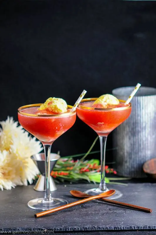 Strawberry Rhubarb Daiquiri Float with ice cream in coupes. Gold dot straws. Wooden spoons. Flowers, jigger and metal container in background